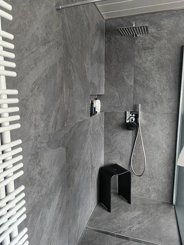 Dusche mit grauen Naturfliesen und Duschhocker